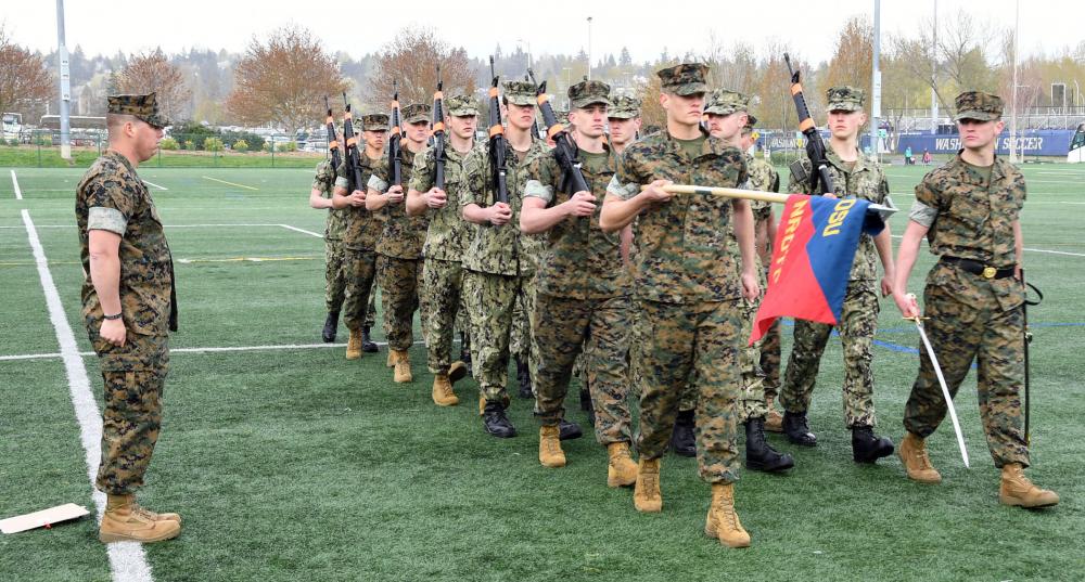 Students marching drill formation with a flag