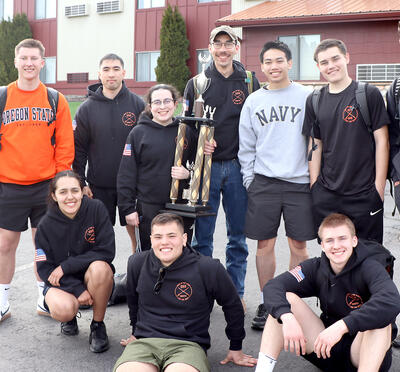 Students standing around a tall trophy in front of a hotel. 
