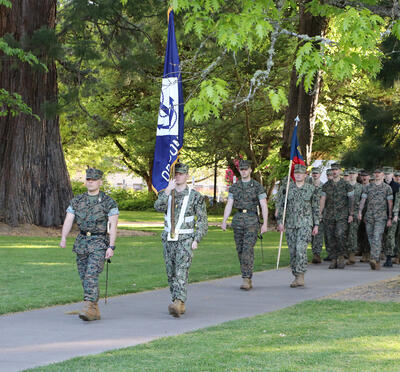Soldiers marching with an OSU and a Navy flag. 
