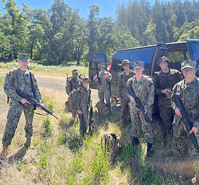 Students in camouflage standing in front of the truck with fake guns. 