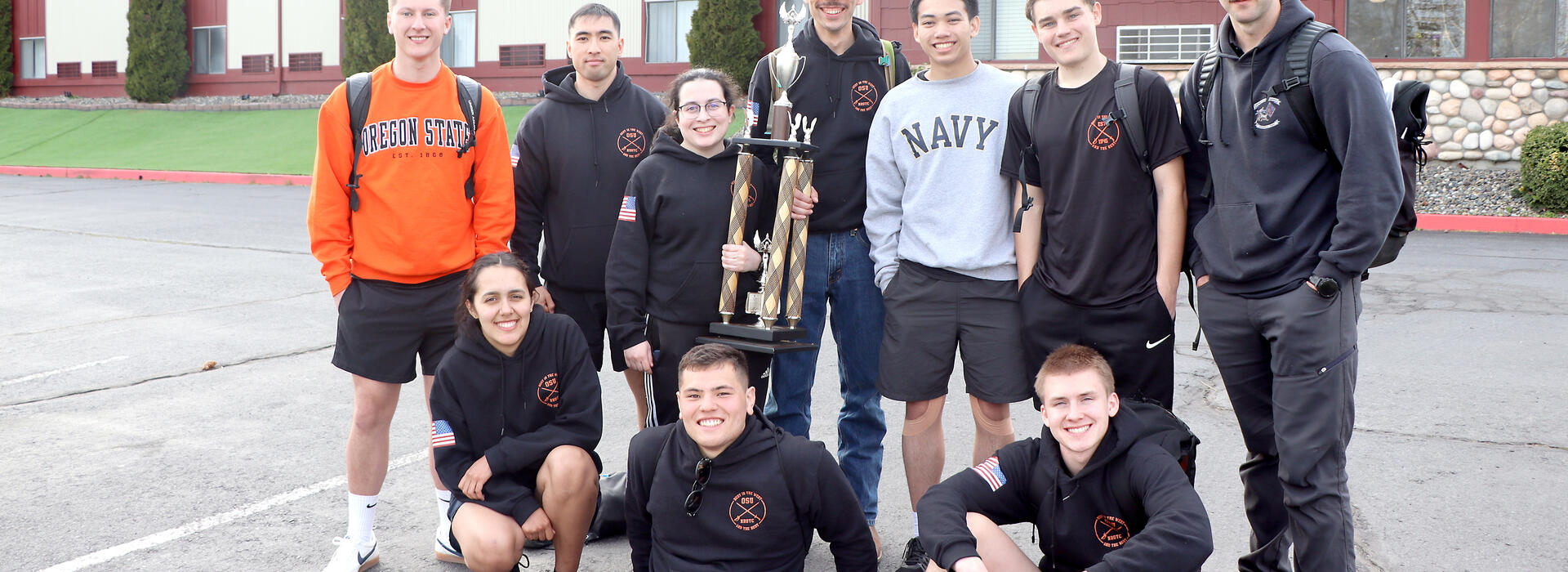 Students standing around a tall trophy in front of a hotel. 