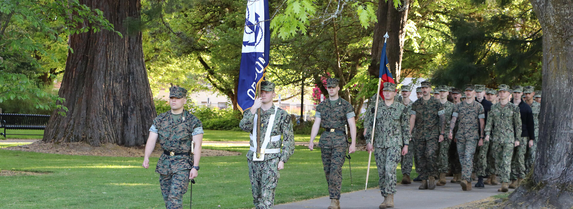 Soldiers marching with an OSU and a Navy flag. 