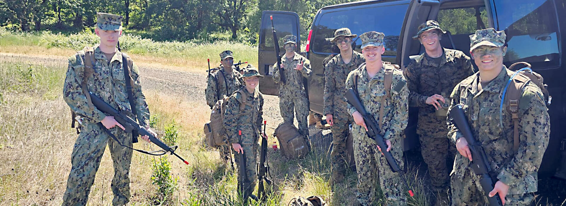 Students in camouflage standing in front of the truck with fake guns. 