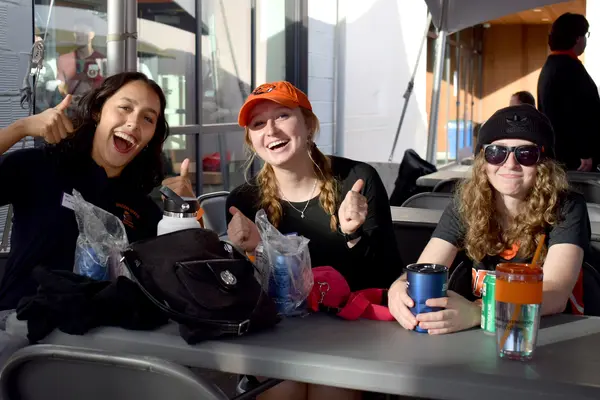 3 students laughing and smiling sitting at a table in OSU shirts