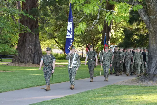 Soldiers marching with an OSU and a Navy flag. 