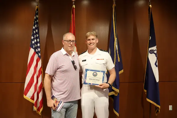 Student and his father pose in front of national flags holding an award.